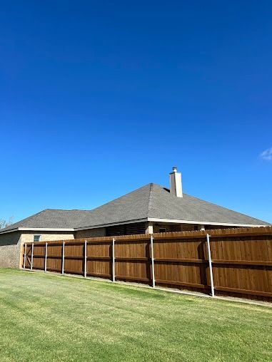 Brown wooden fence surrounding a house with a gray roof and a clear blue sky.