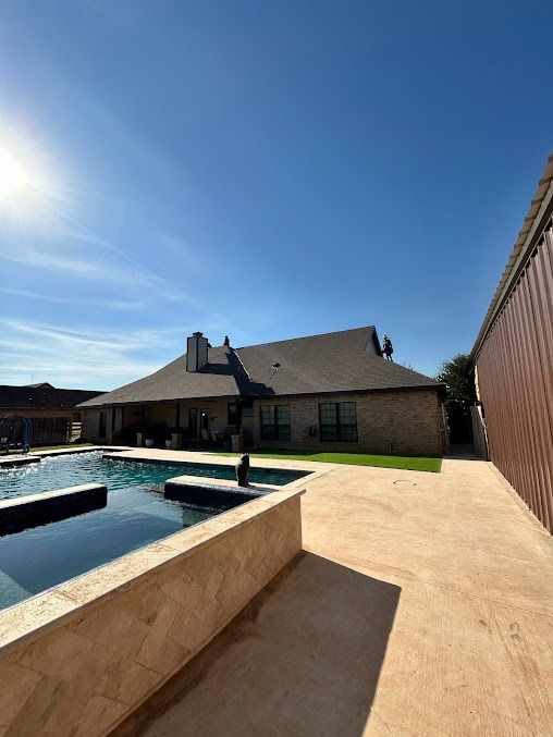 Backyard with a swimming pool, house, concrete patio, and blue sky.