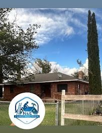 A one-story brick house with the N&E Construction logo in the foreground, under a blue sky.