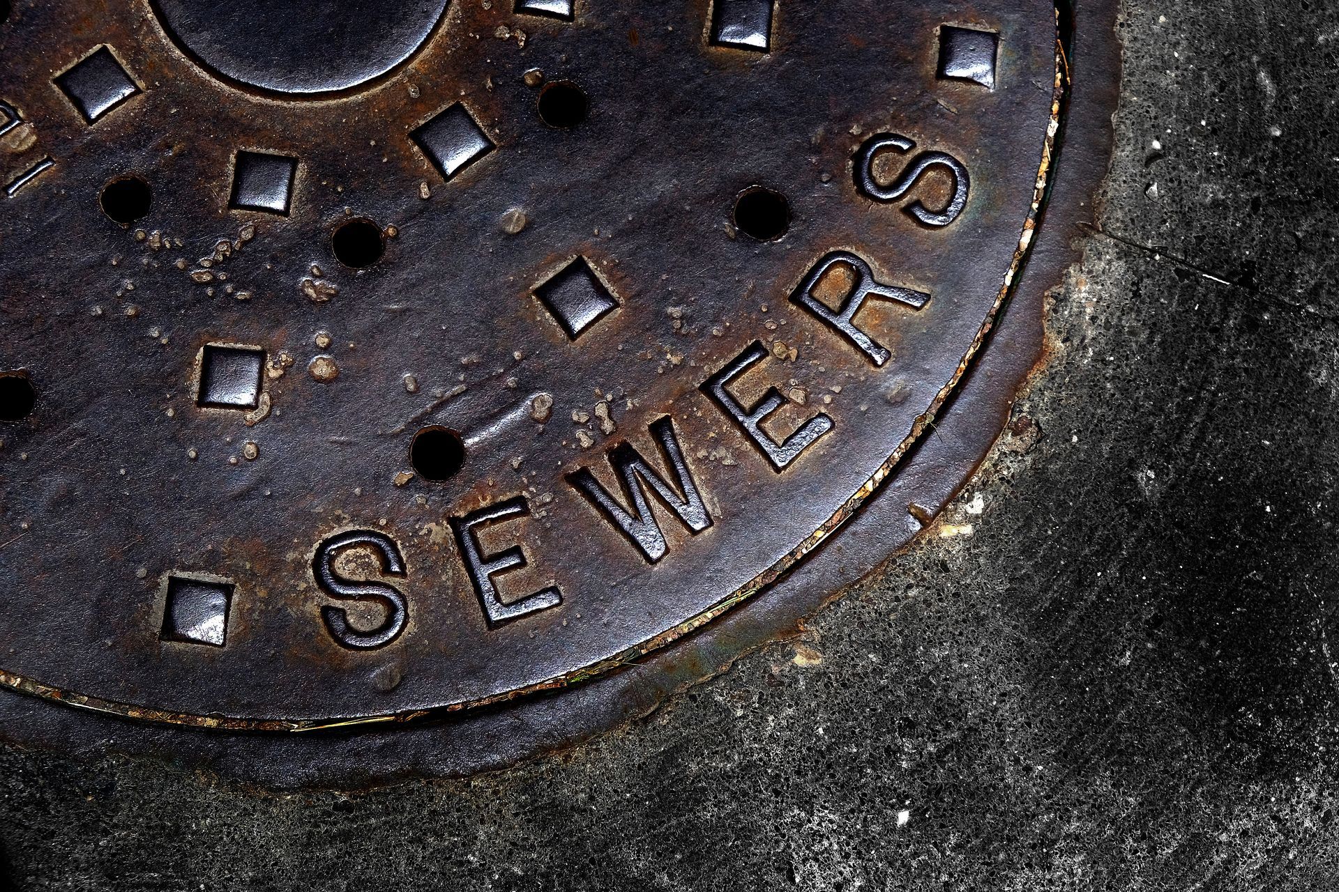 Rusty manhole cover with “SEWERS” text embedded in pavement.
