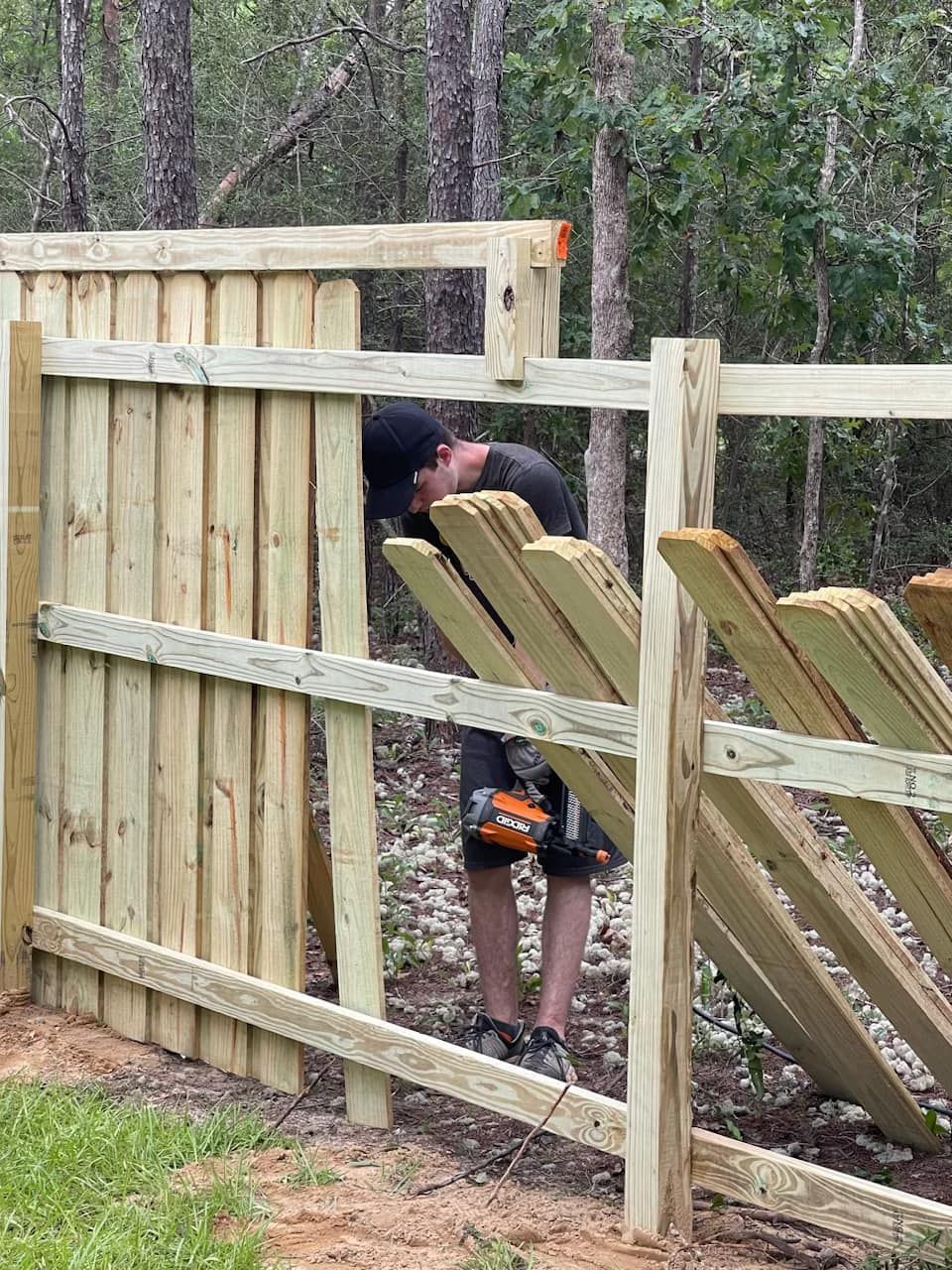 A man is working on a wooden fence in the woods.