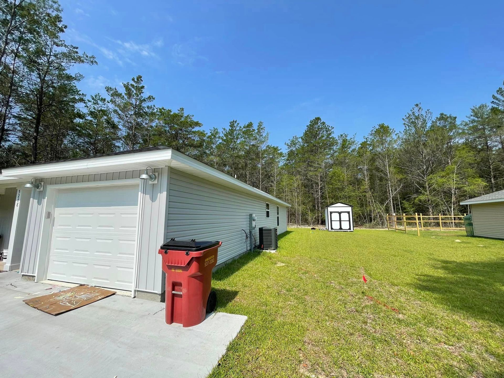 A white garage with a red trash can in front of it.
