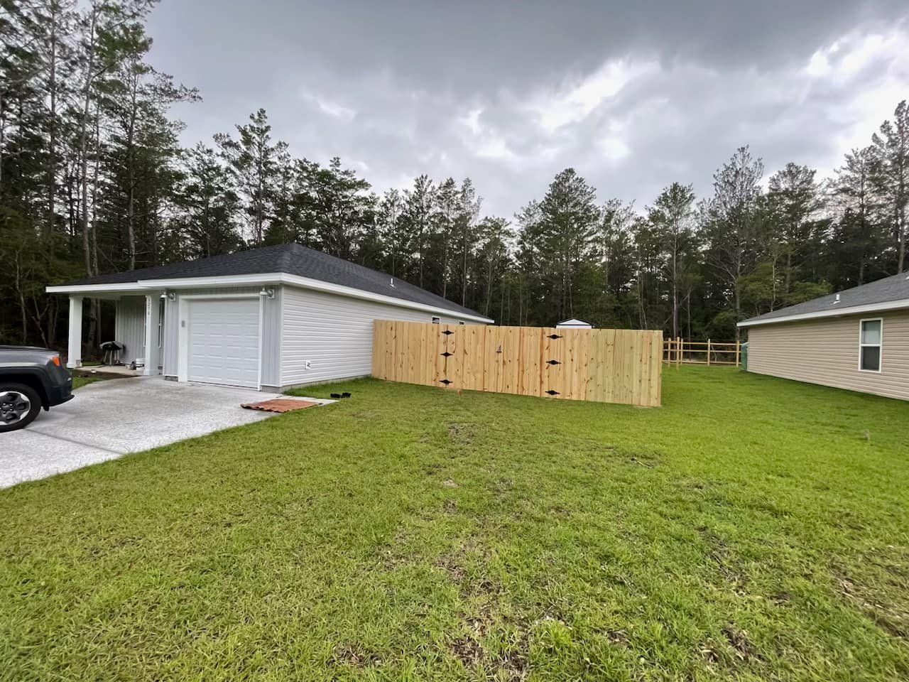 A car is parked in front of a house with a wooden fence.