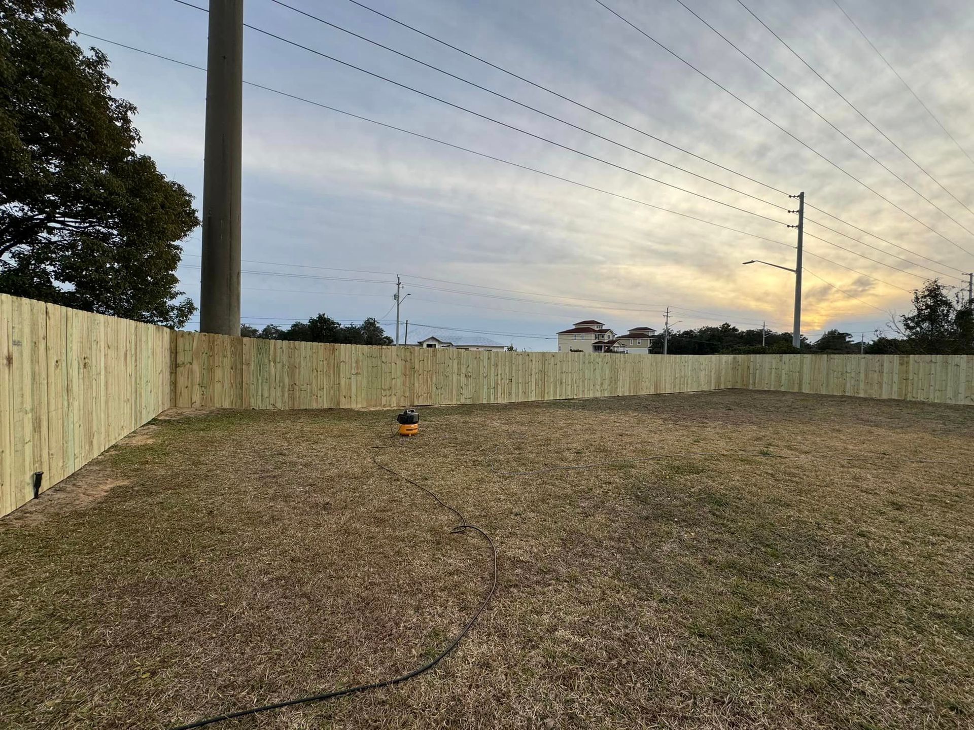 A wooden fence surrounds a grassy field with power lines in the background.