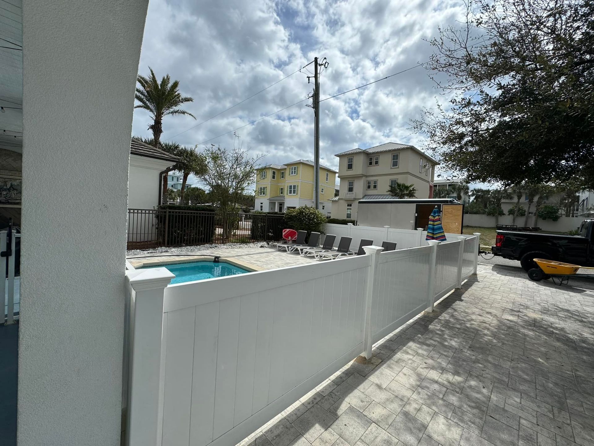A white fence surrounds a swimming pool in front of a house.