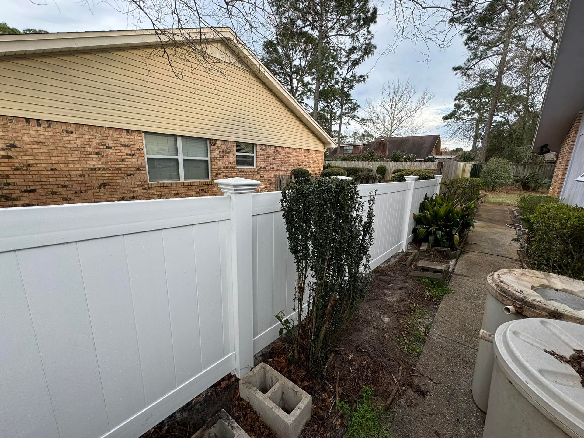 A white fence surrounds a brick house in a backyard.