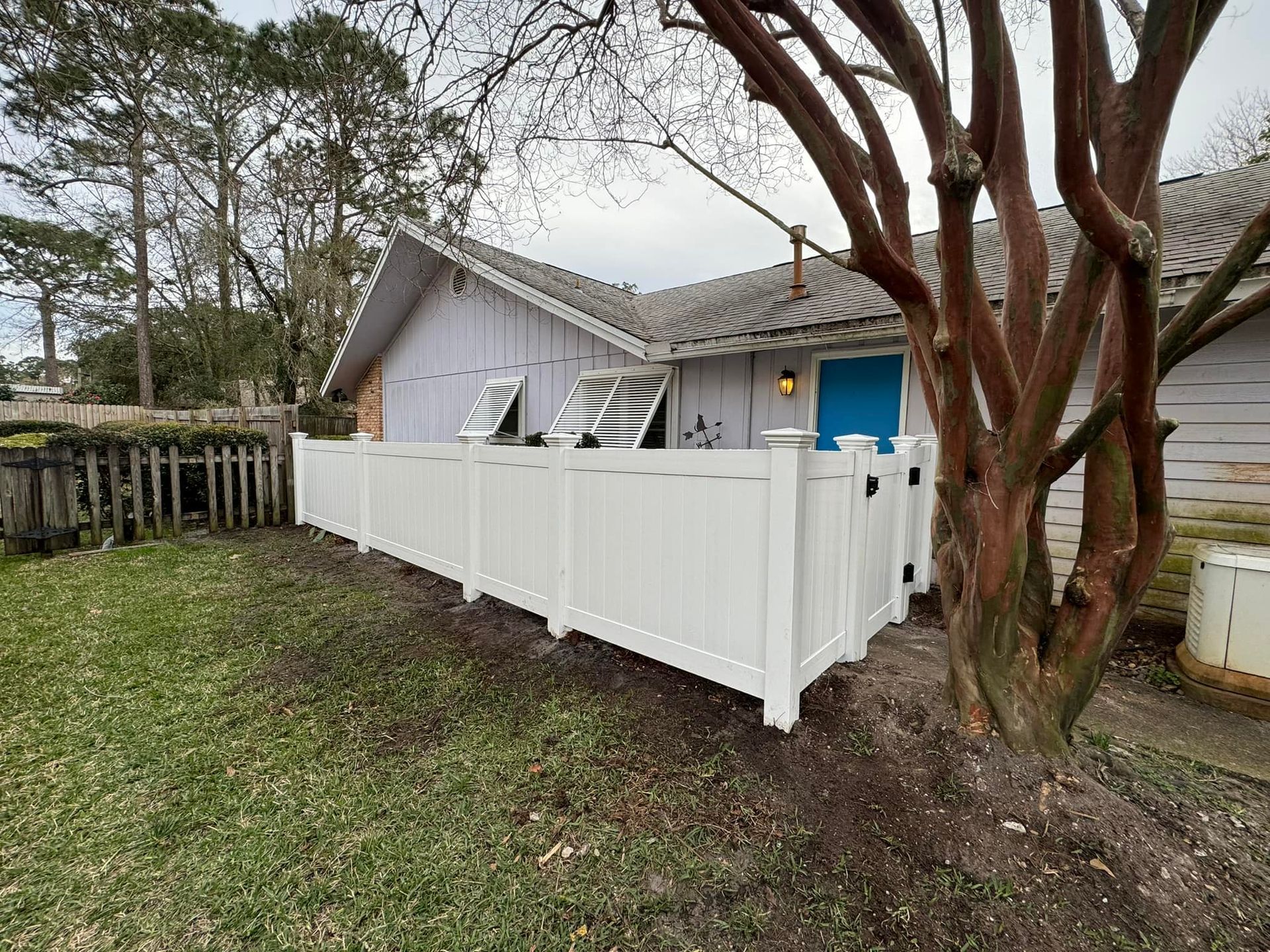 A white fence is in front of a house with a blue door.
