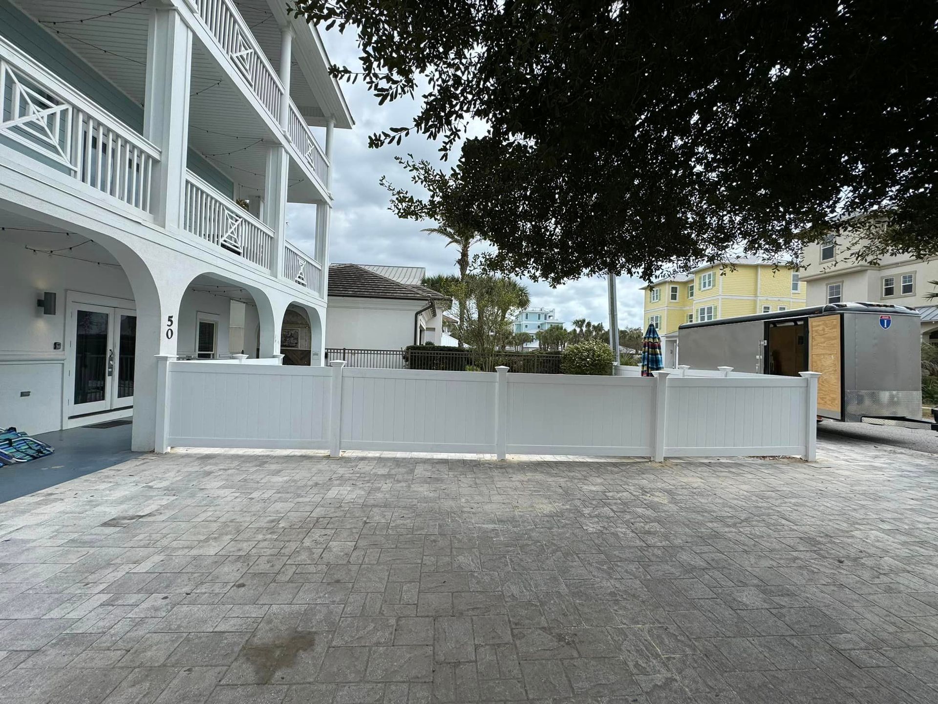 A white fence is surrounding a parking lot in front of a building.
