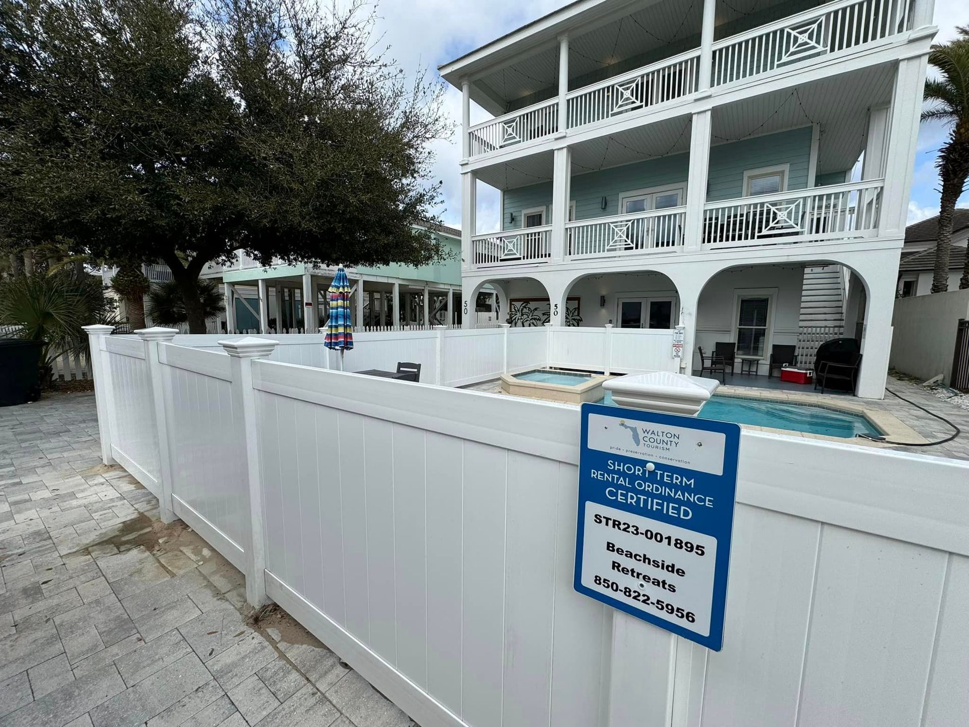 A white fence surrounds a large house with a pool.