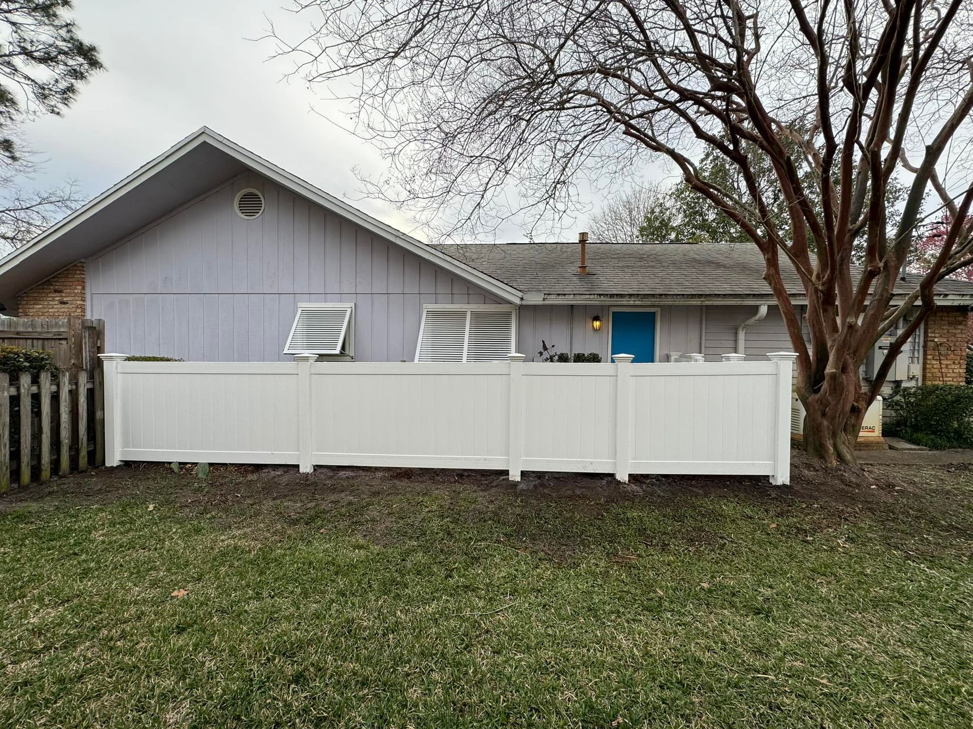 A white fence is in front of a house with a blue door.