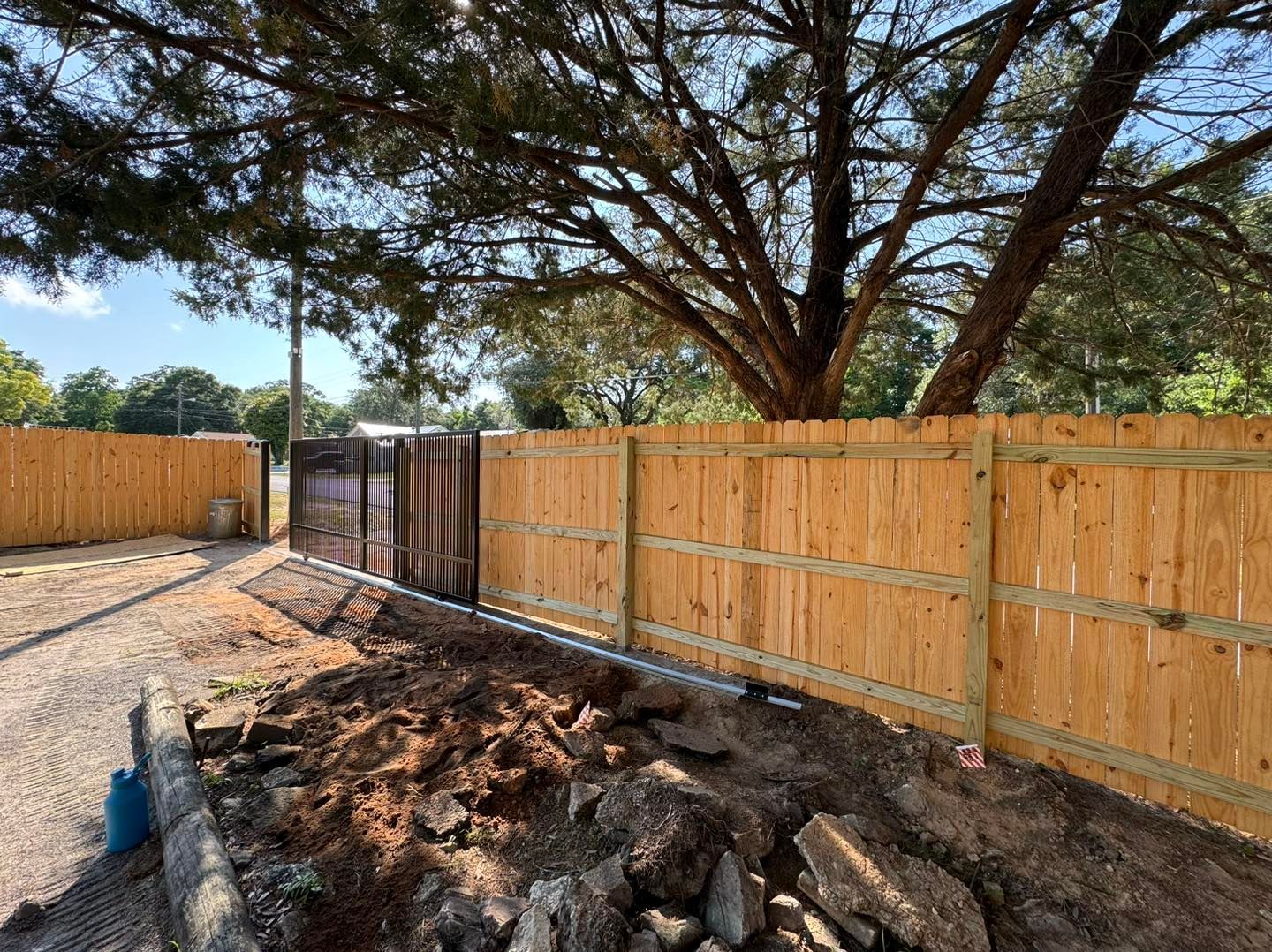 A wooden fence is being built in a backyard with a tree in the background.