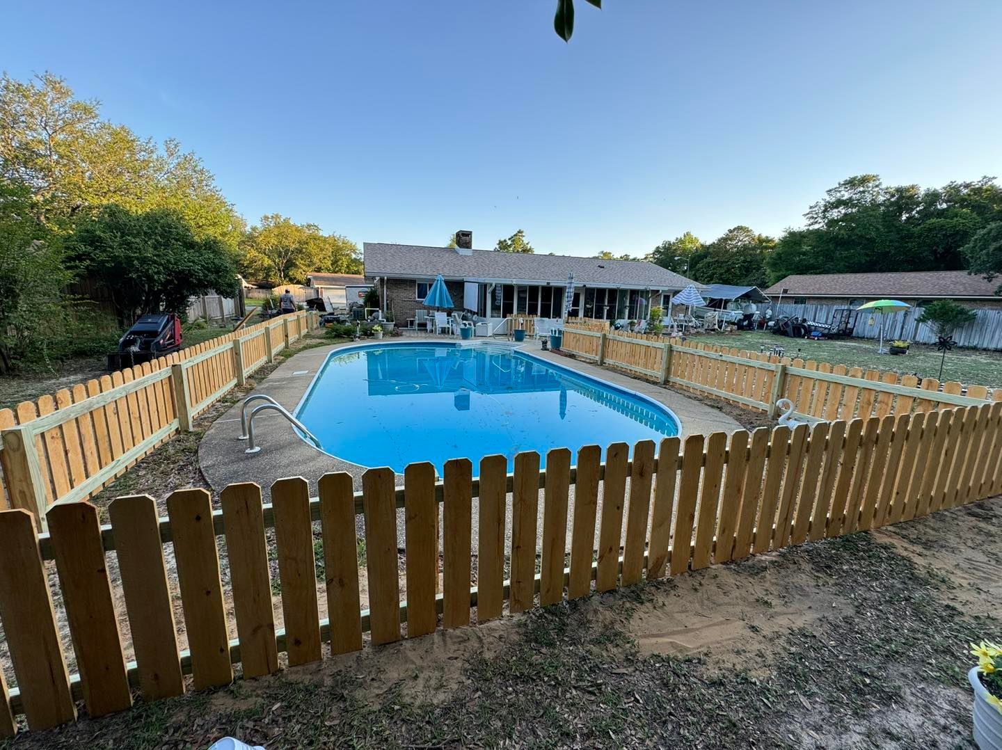 A wooden fence surrounds a swimming pool in front of a house.