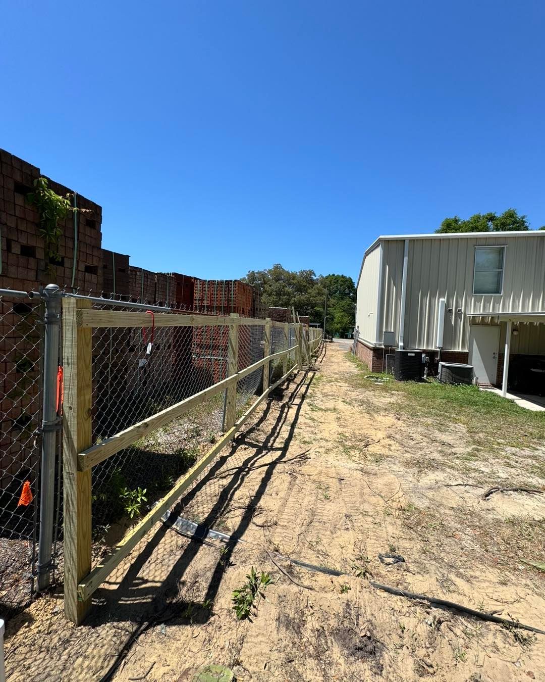 A wooden fence surrounds a dirt road in front of a house.