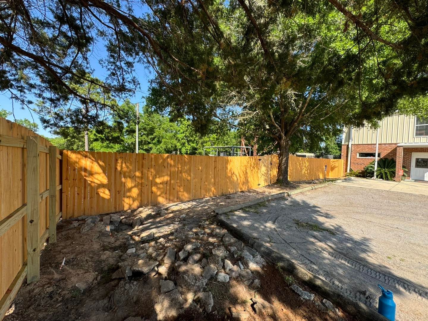 A wooden fence is surrounding a dirt area in front of a house.
