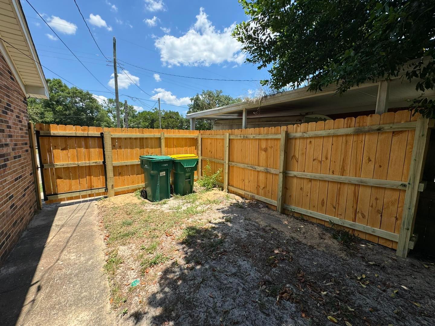 A wooden fence with two trash cans in the backyard of a house.