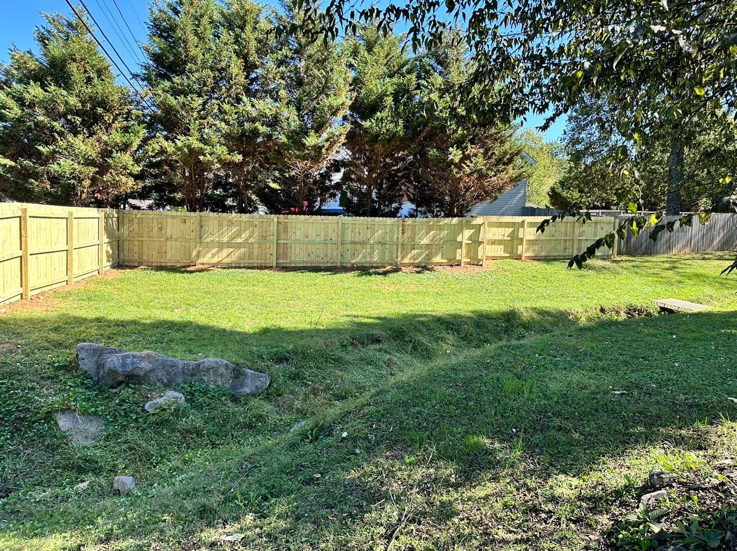 A backyard with a wooden fence and trees in the background.