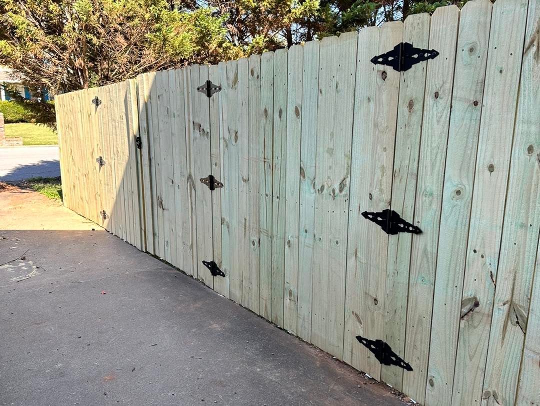 A wooden fence with black hinges is sitting on the side of a road.