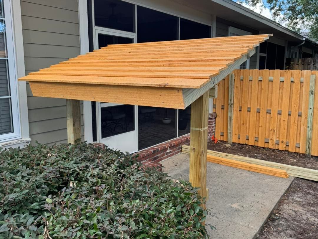 A wooden canopy is sitting in front of a house next to a wooden fence.
