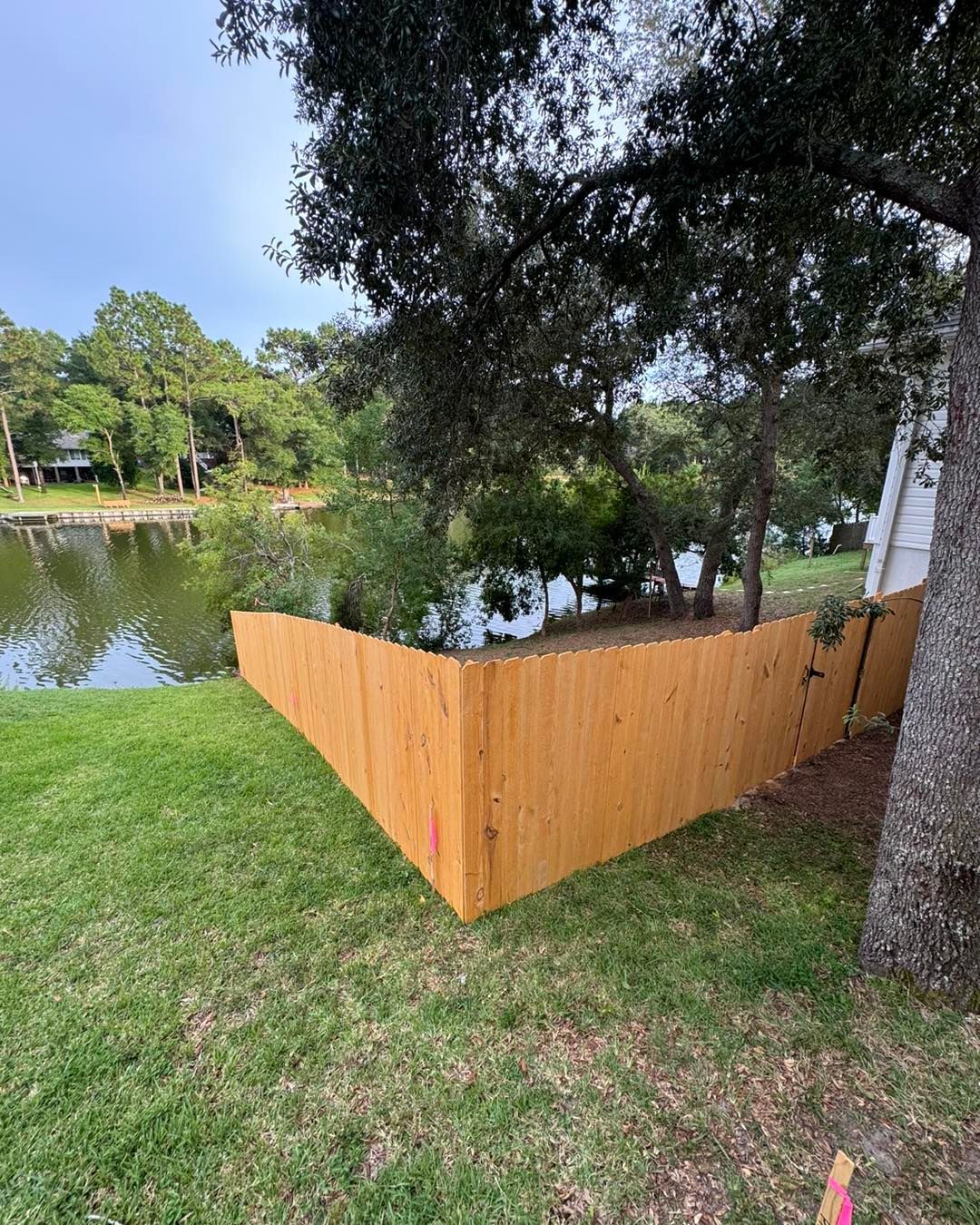 A wooden fence is in the middle of a lush green field next to a lake.