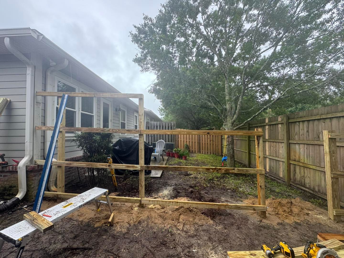 A wooden fence is being built in the backyard of a house.
