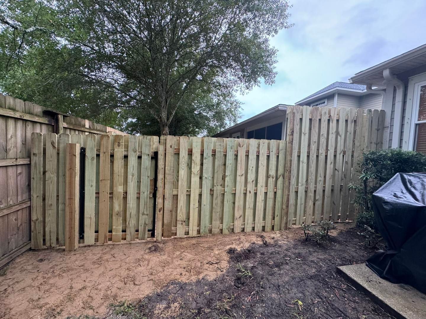 A wooden fence is in the backyard of a house.