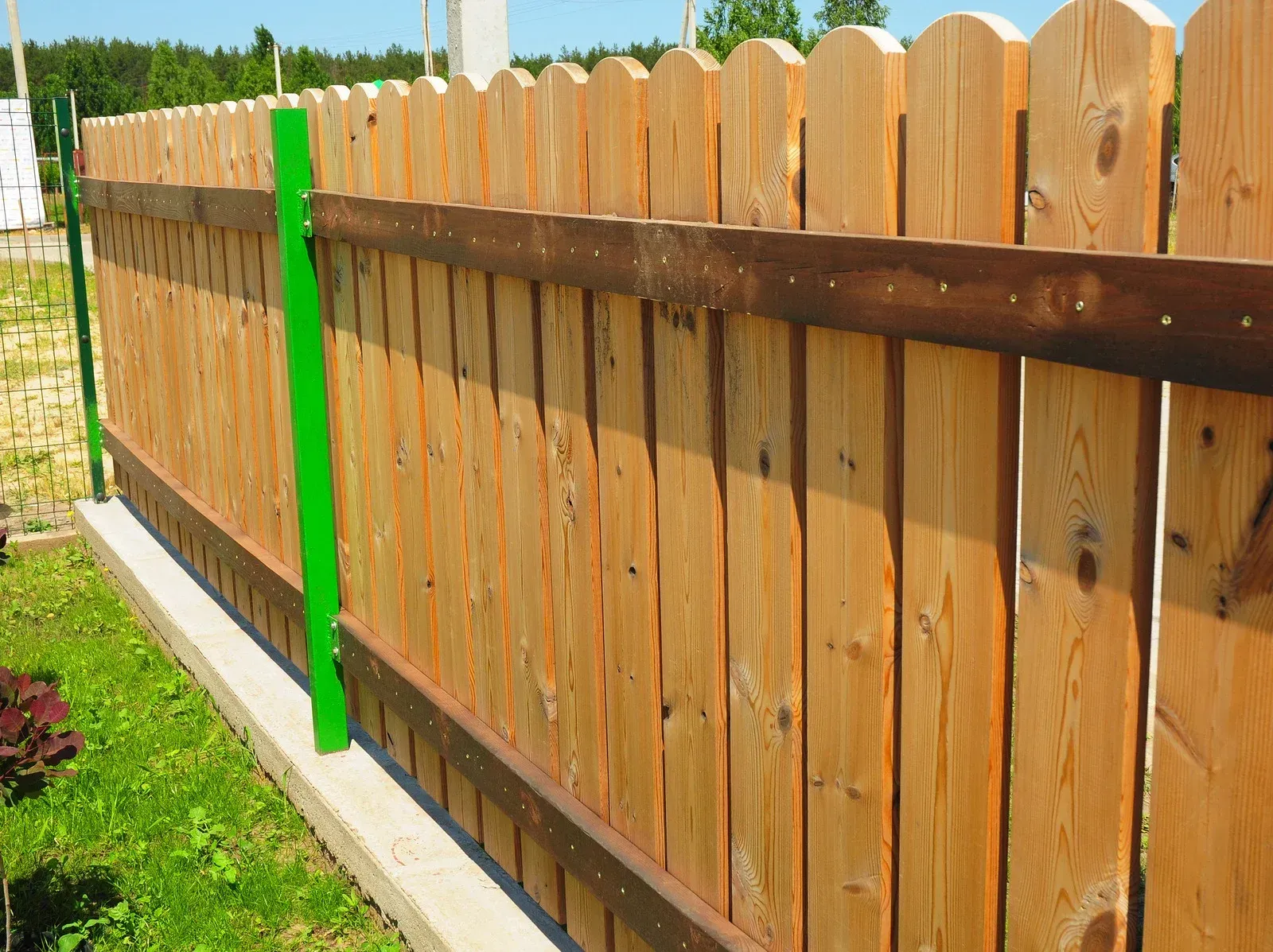 Wooden picket fence with dark brown horizontal beams and bright green posts, outdoors.