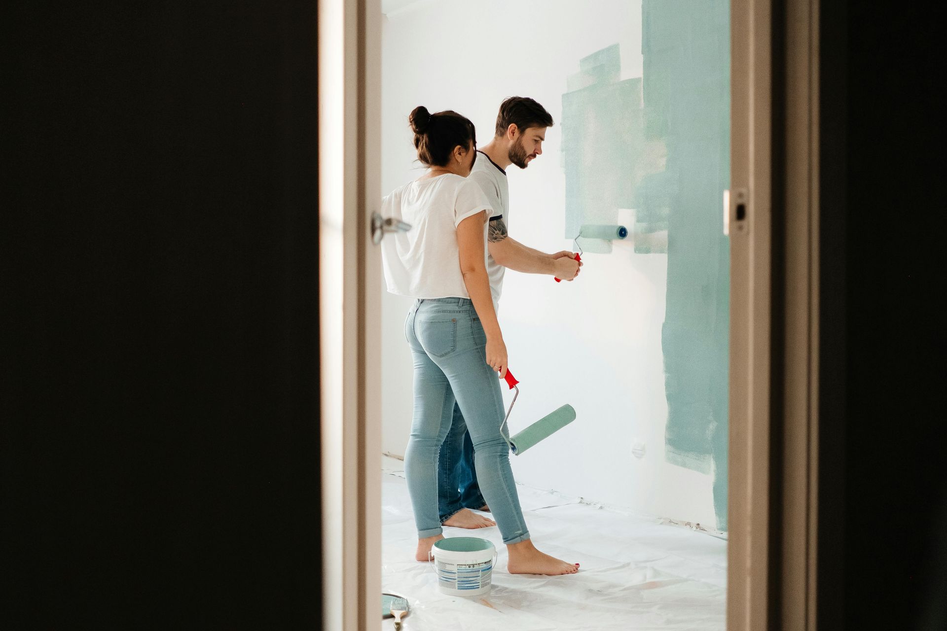 Couple painting a wall light blue in a room; the woman holds a roller, the man paints.