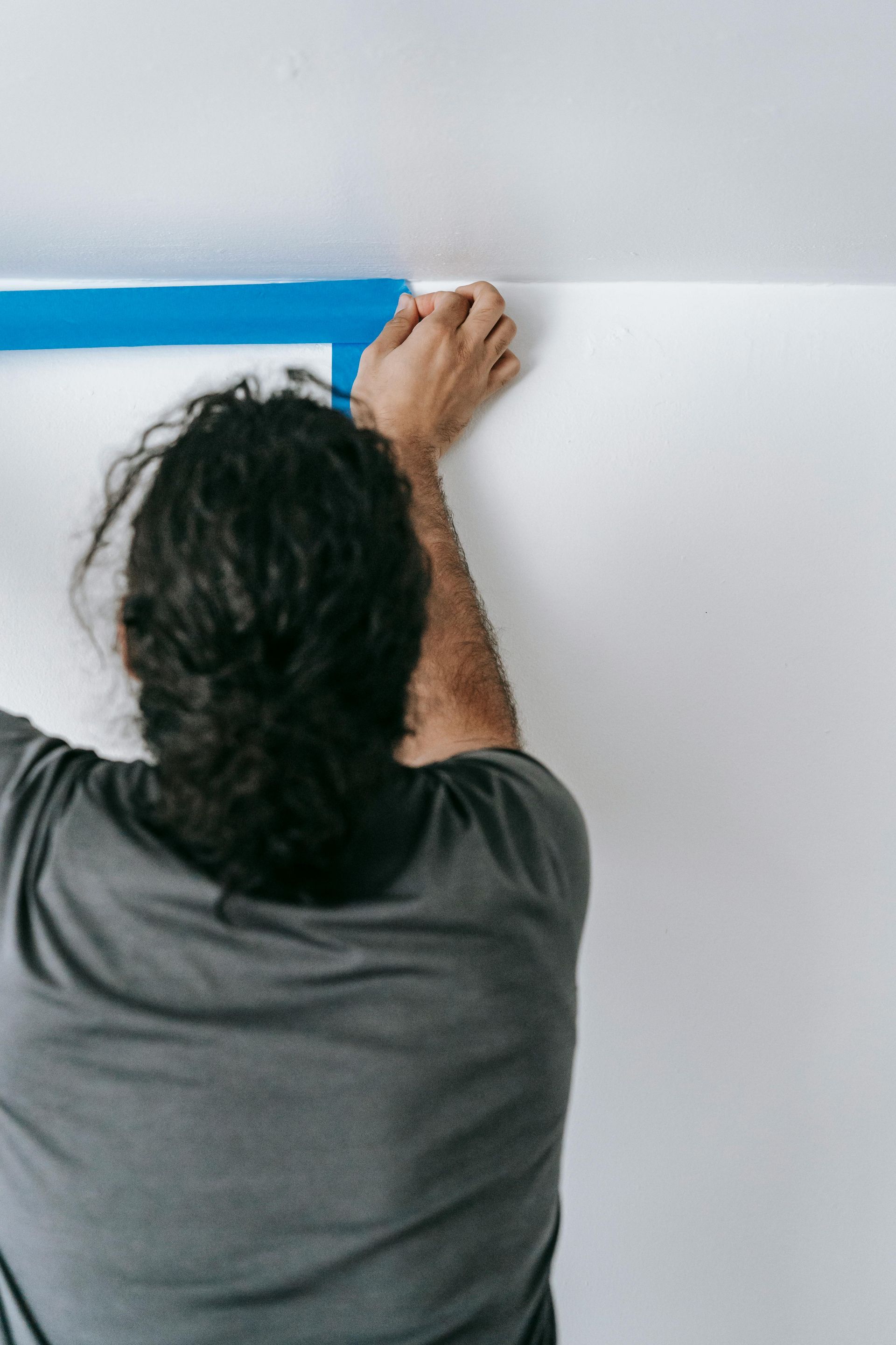 Person applies blue painter's tape to a wall near a ceiling.