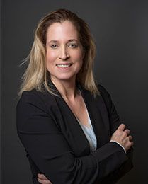 A woman in a black jacket is smiling with her arms crossed.