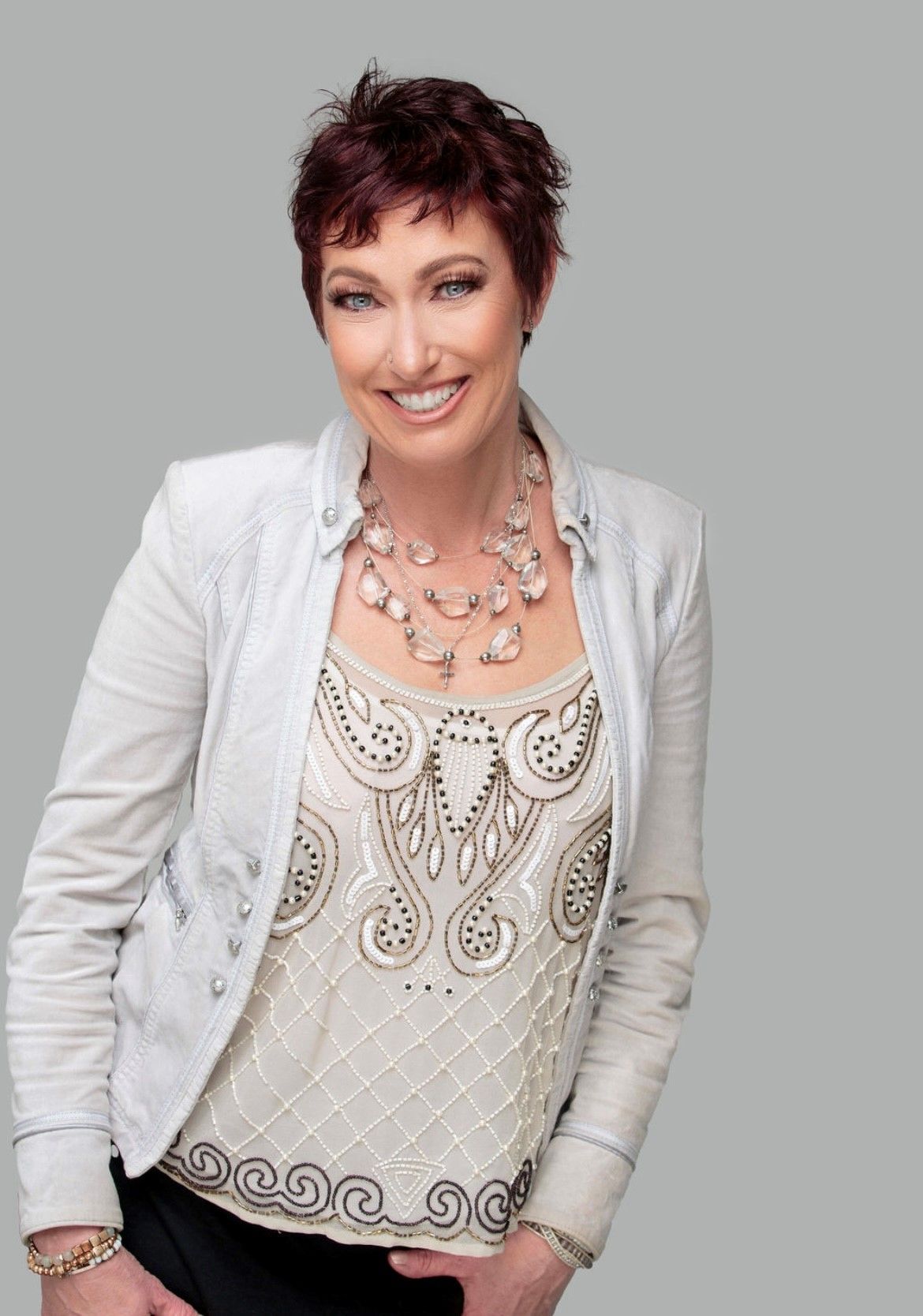 A woman wearing a white jacket and a white top is smiling.