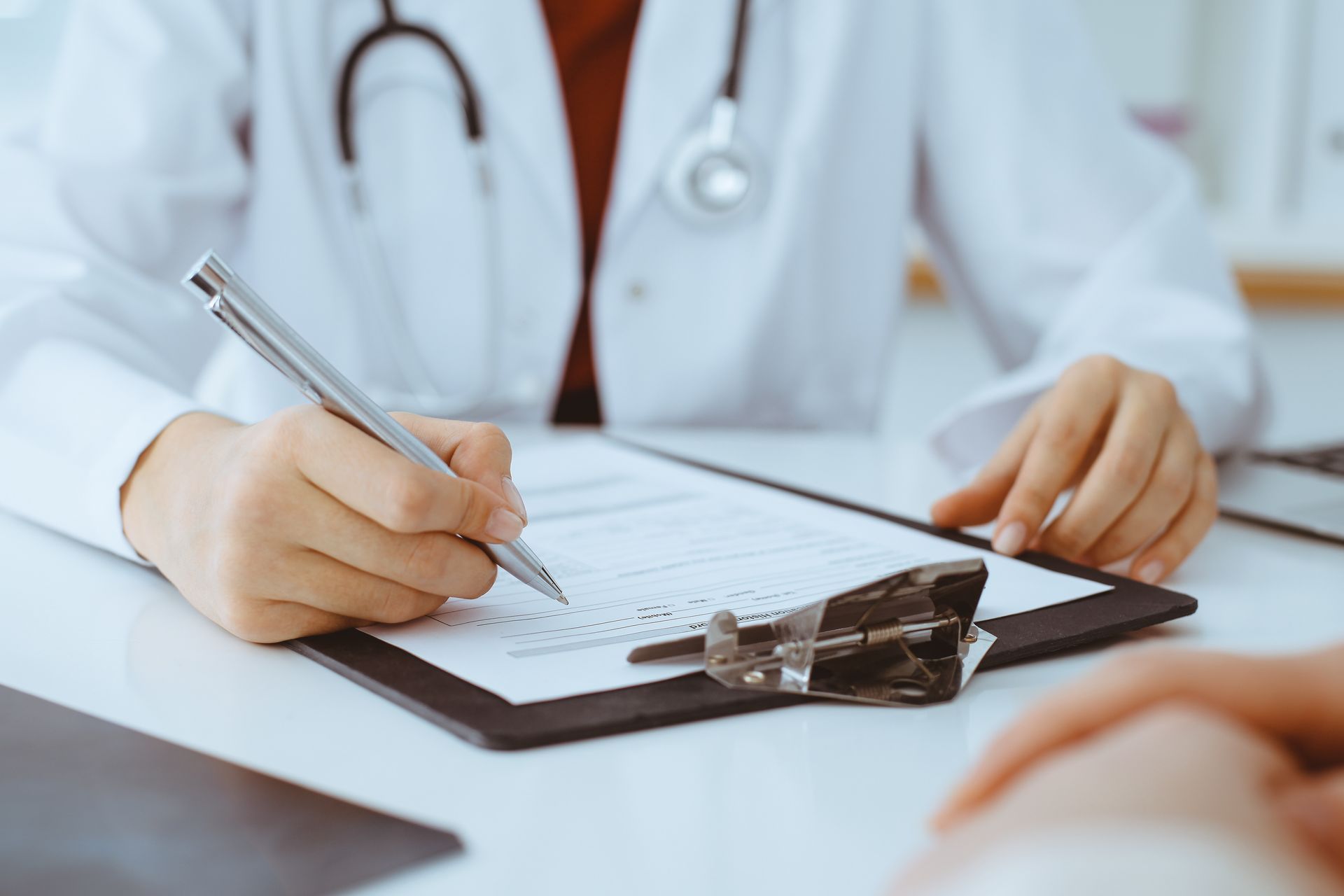 A doctor is writing on a clipboard while talking to a patient.