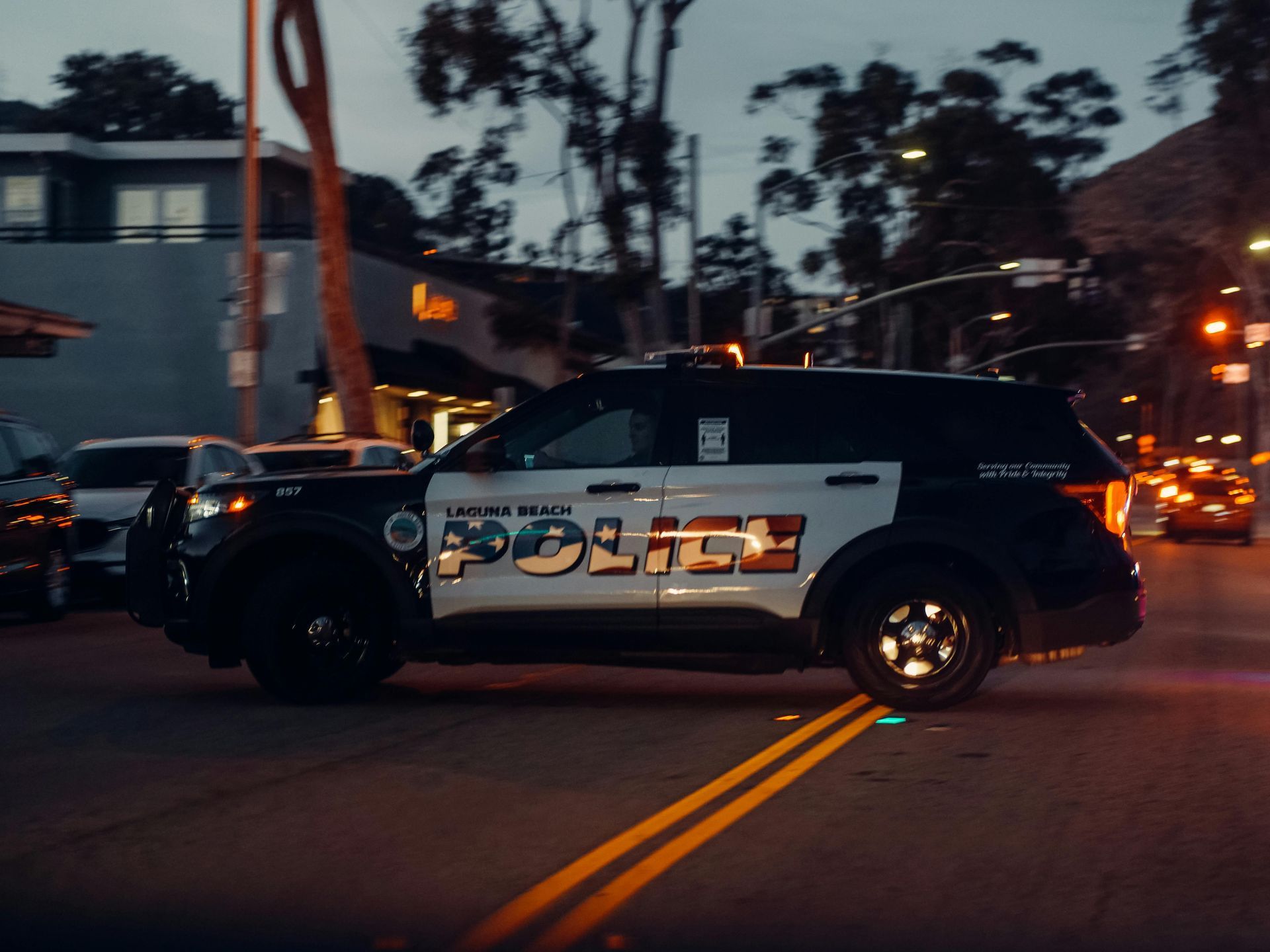 A Laguna Beach police SUV driving across a street intersection during twilight.