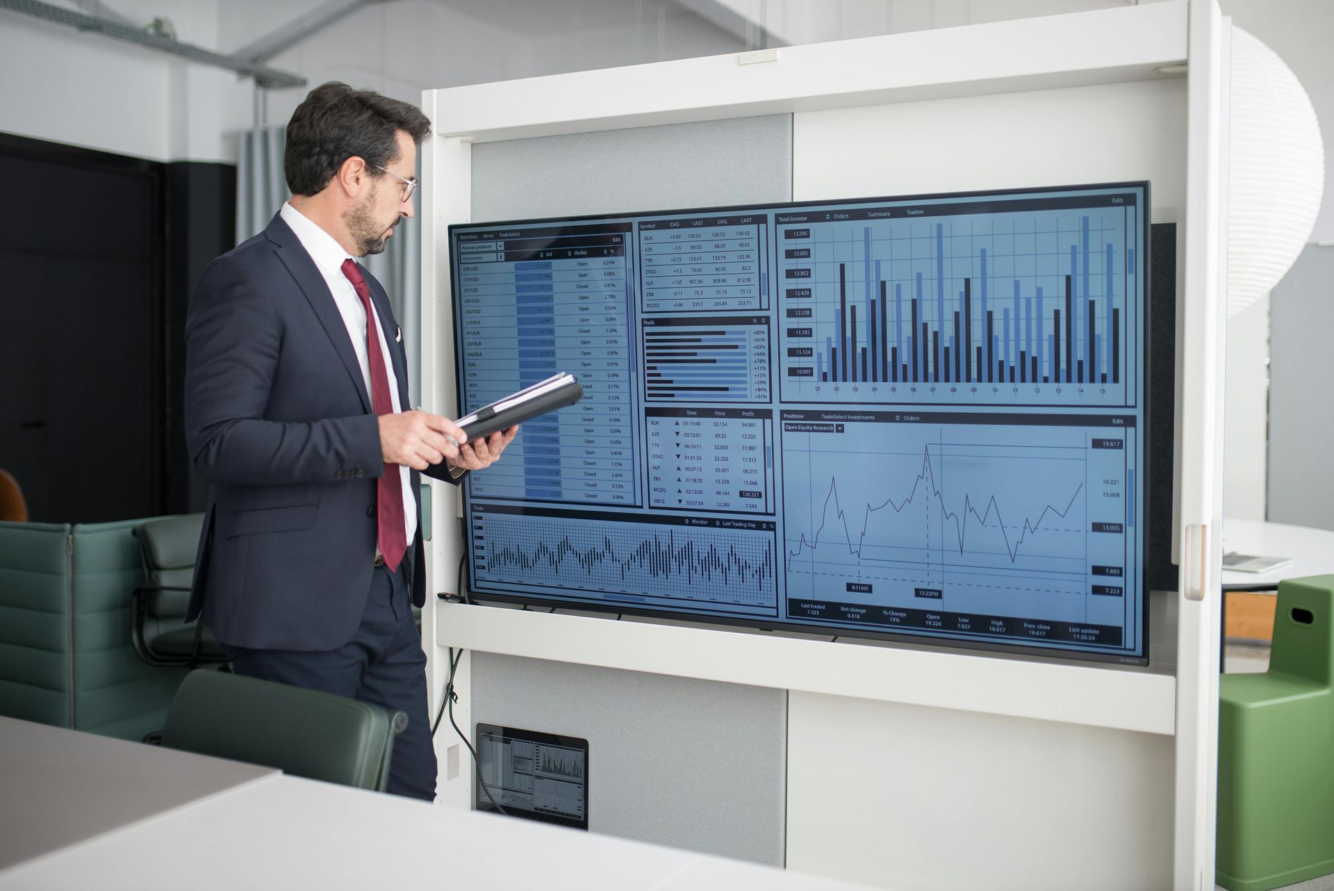 Man in suit examines data on multiple screens in a modern office.