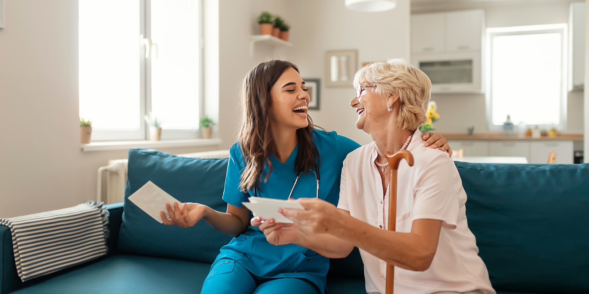 Healthcare provider in blue scrubs with stethoscope, comforts older man in light blue shirt, both smiling.