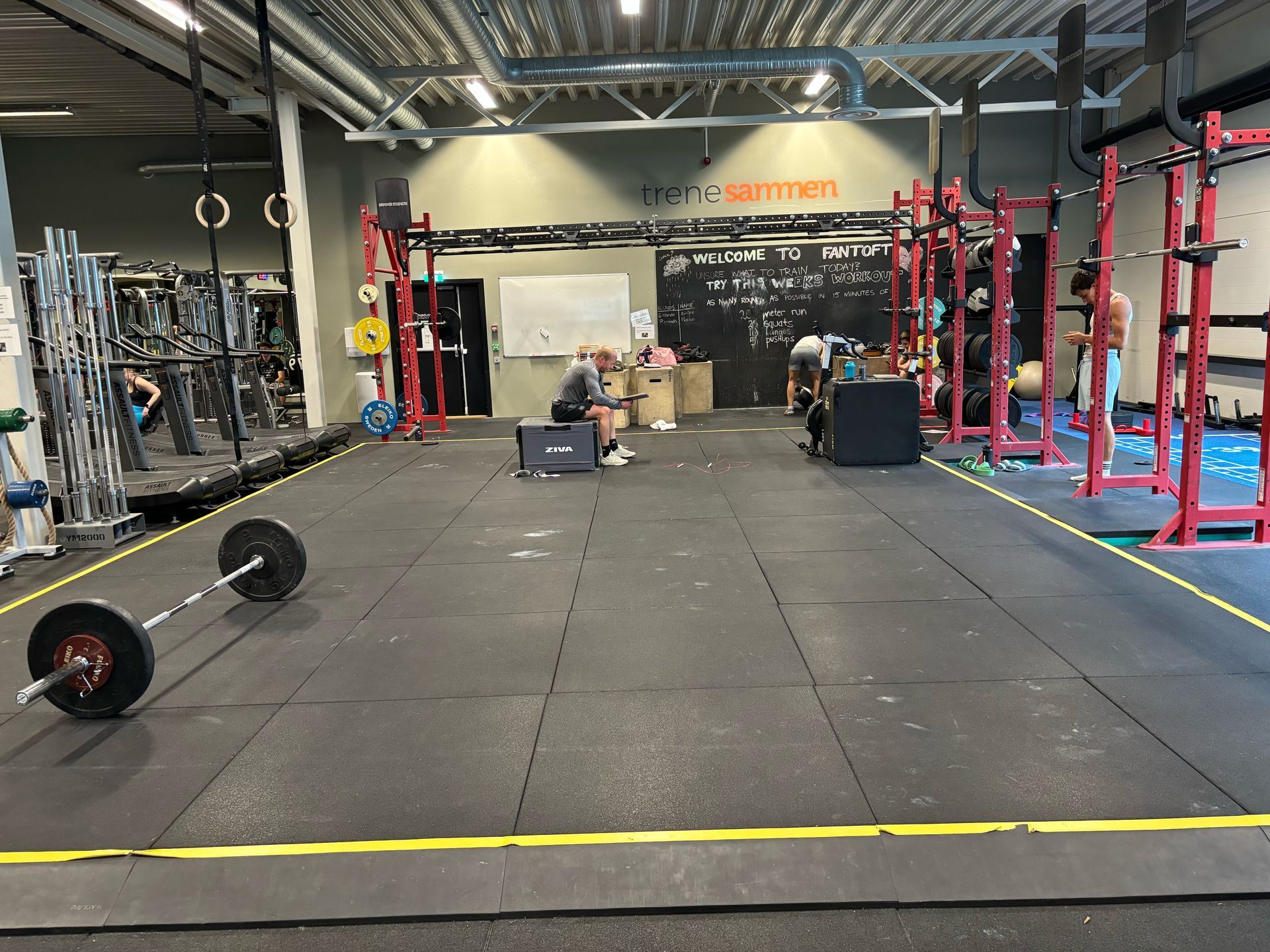 Weightlifting gym interior with equipment and people working out. Black floor, red metal frames.