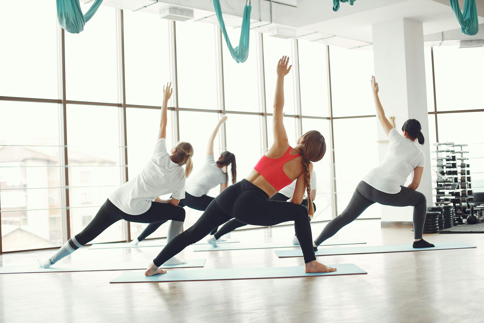 Three people in a bright studio perform yoga side stretches on mats.