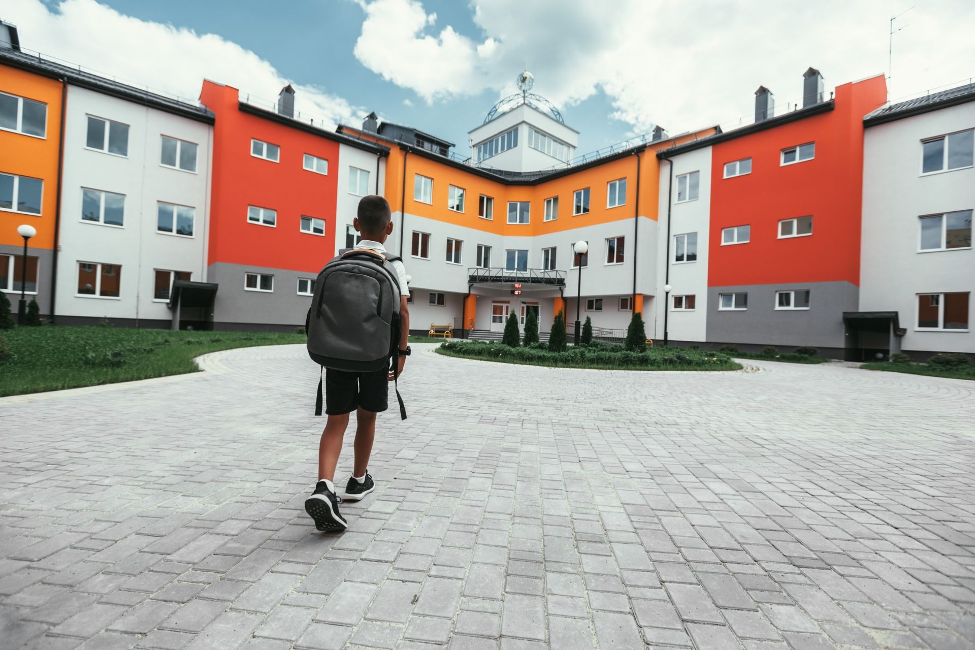 A boy with a backpack is walking towards a school building.