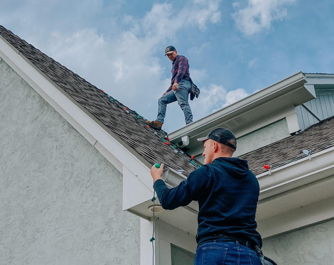 two men are hanging Christmas lights on a house.