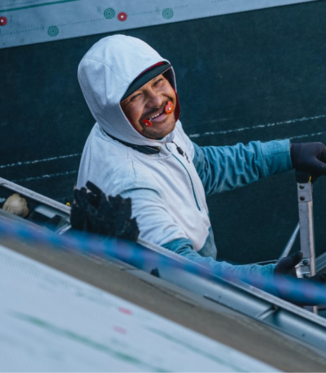 a man wearing a hooded jacket and working on a roof is smiling.