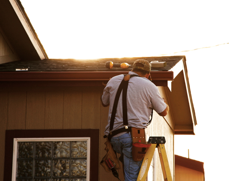 a man is standing on a ladder working on the gutters of a house.