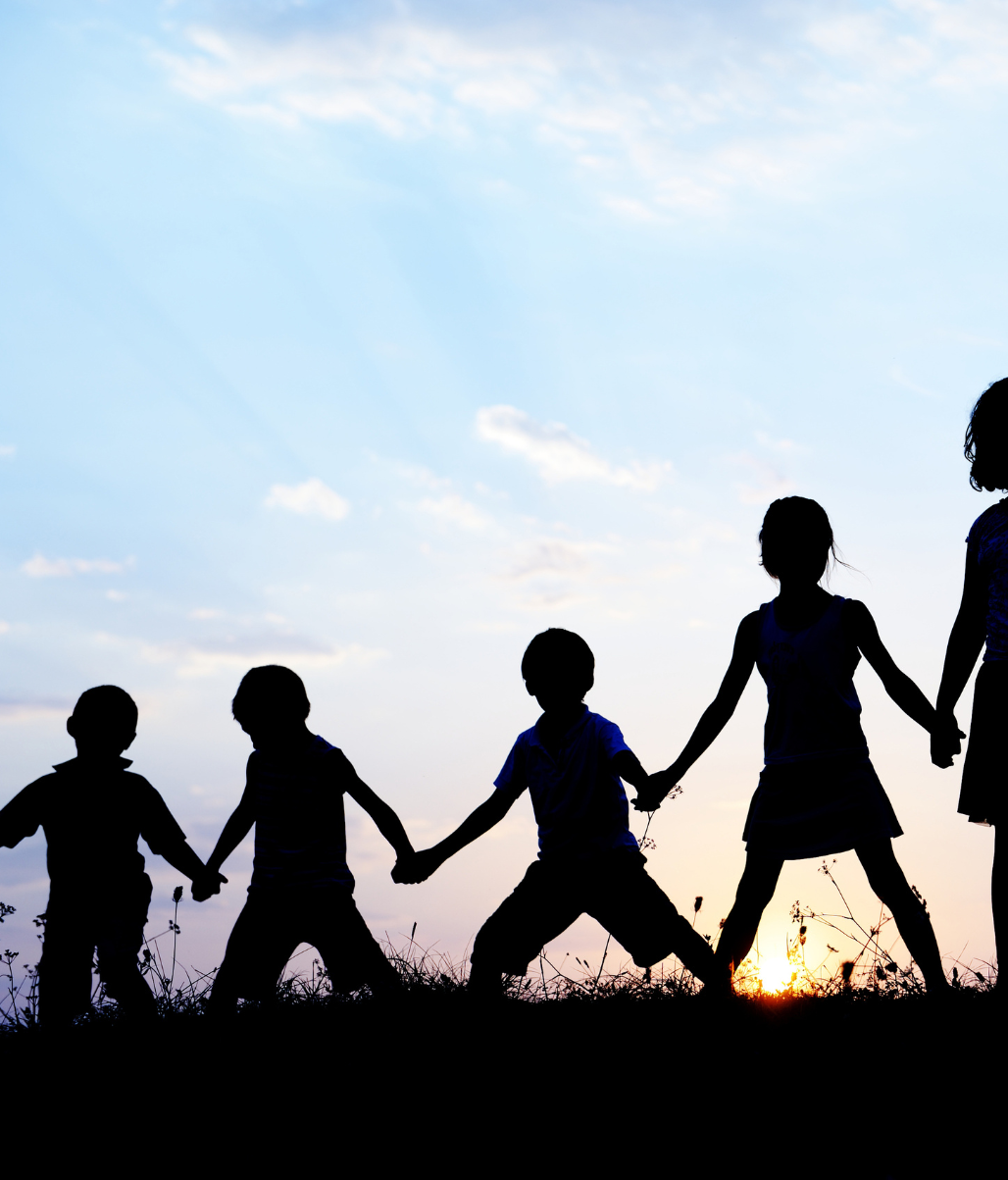a group of children holding hands in a field at sunset.