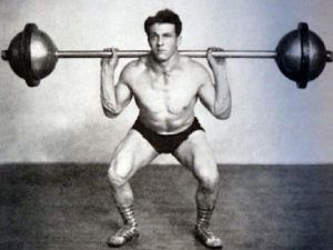 A man is squatting with a barbell on his shoulders.