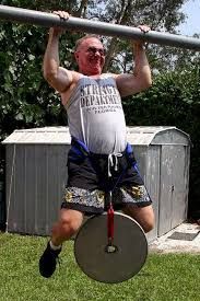 A man is doing a pull up on a bar in a yard.