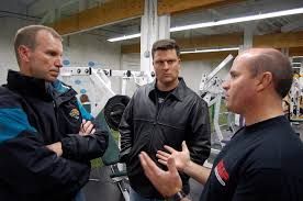 Three men are standing in a gym talking to each other.