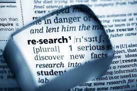 A magnifying glass is looking at the word research in a dictionary.