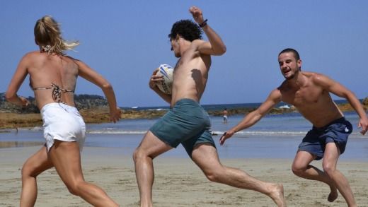 A group of people are playing rugby on the beach.