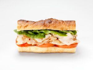 A sandwich with turkey , lettuce and tomatoes on a white surface.