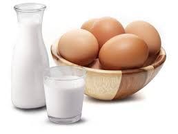 A bowl of eggs next to a glass of milk and a bottle of milk.