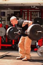 A man is lifting a barbell in a garage.