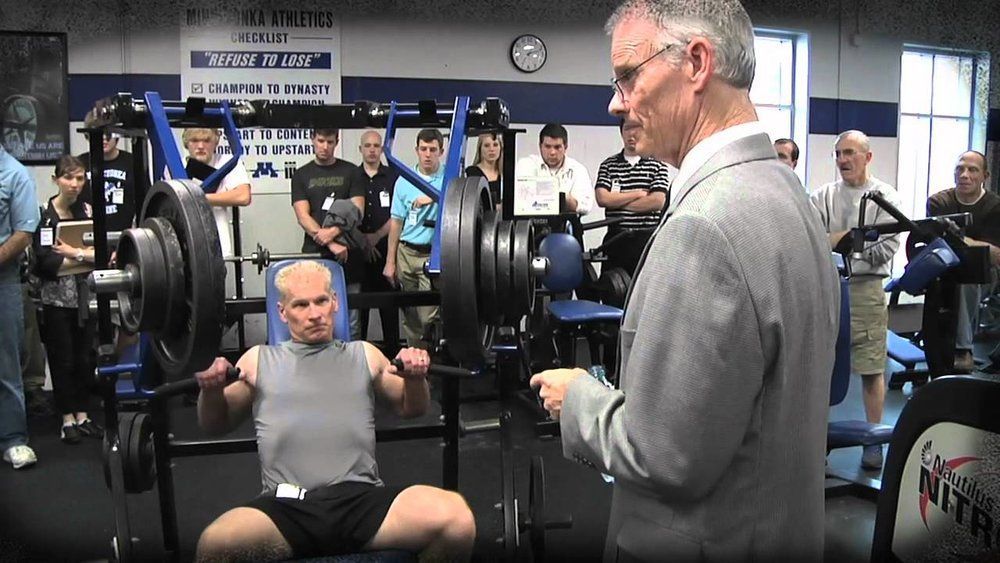 A man is squatting on a bench in a gym